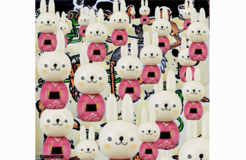Illustration showing many identical white cartoon rabbits wearing pink kimono-like outfits, repeated across the image at different sizes. The rabbits have long ears, small black eyes, and smiling faces with rosy cheeks. They appear layered over a colorful, abstract background with doodle-like shapes and patterns. The rabbits evoke Rabbit RI, a Large Action Model. (Illustration by Francois Top)